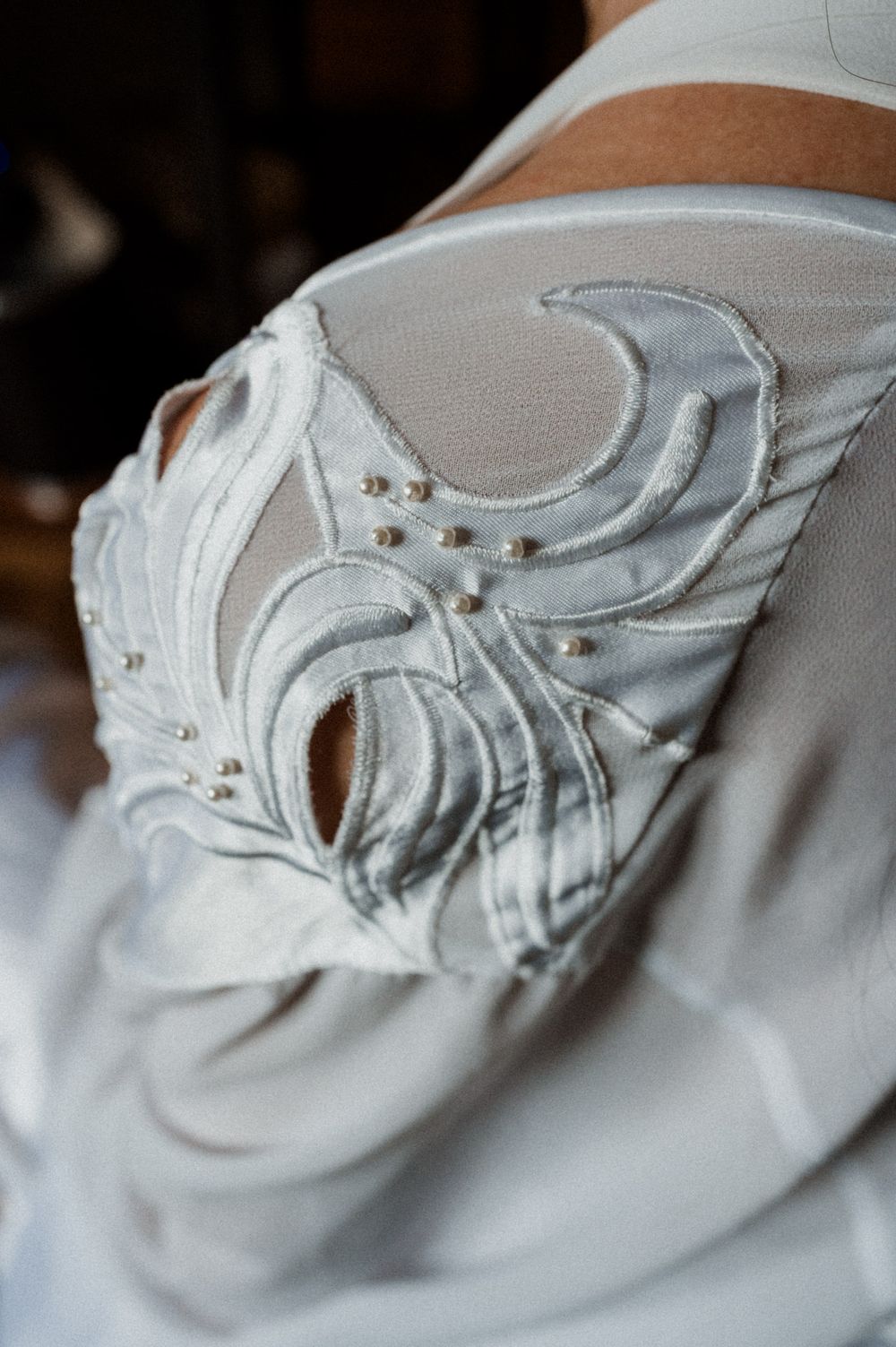 Close-up detail shots of white embroidered fabric with floral pattern and decorative stitching on light colored material.