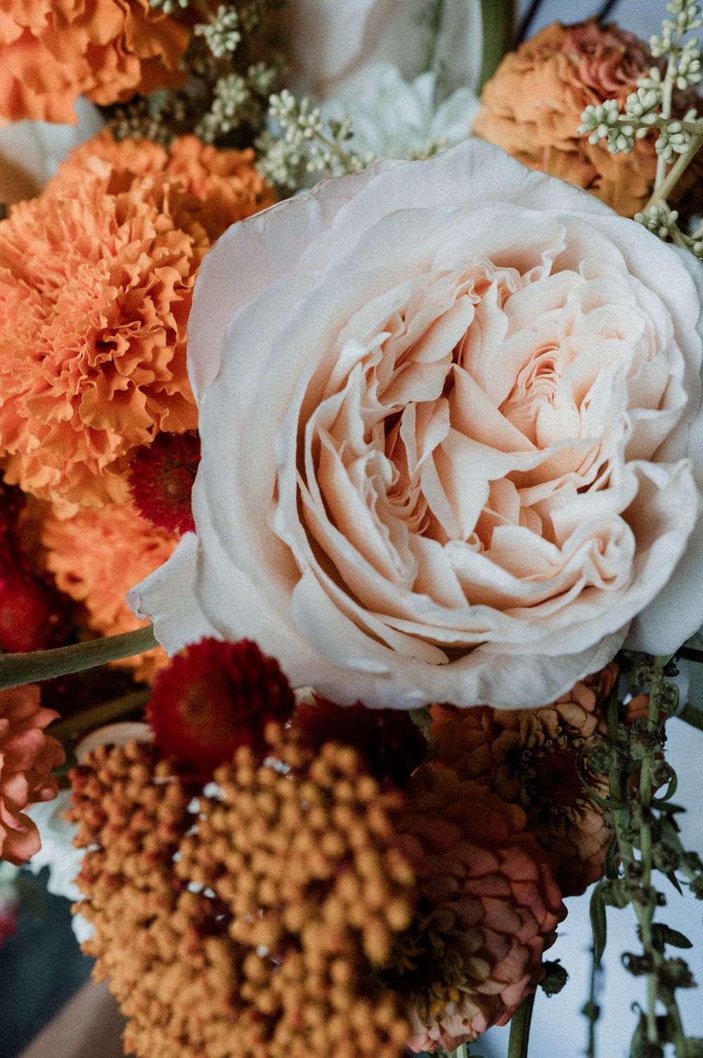 Close-up floral arrangement featuring soft white roses and vibrant orange carnations with delicate baby's breath accents.