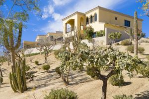 Desert villa with Spanish architecture perched on a hillside surrounded by cacti and desert vegetation.