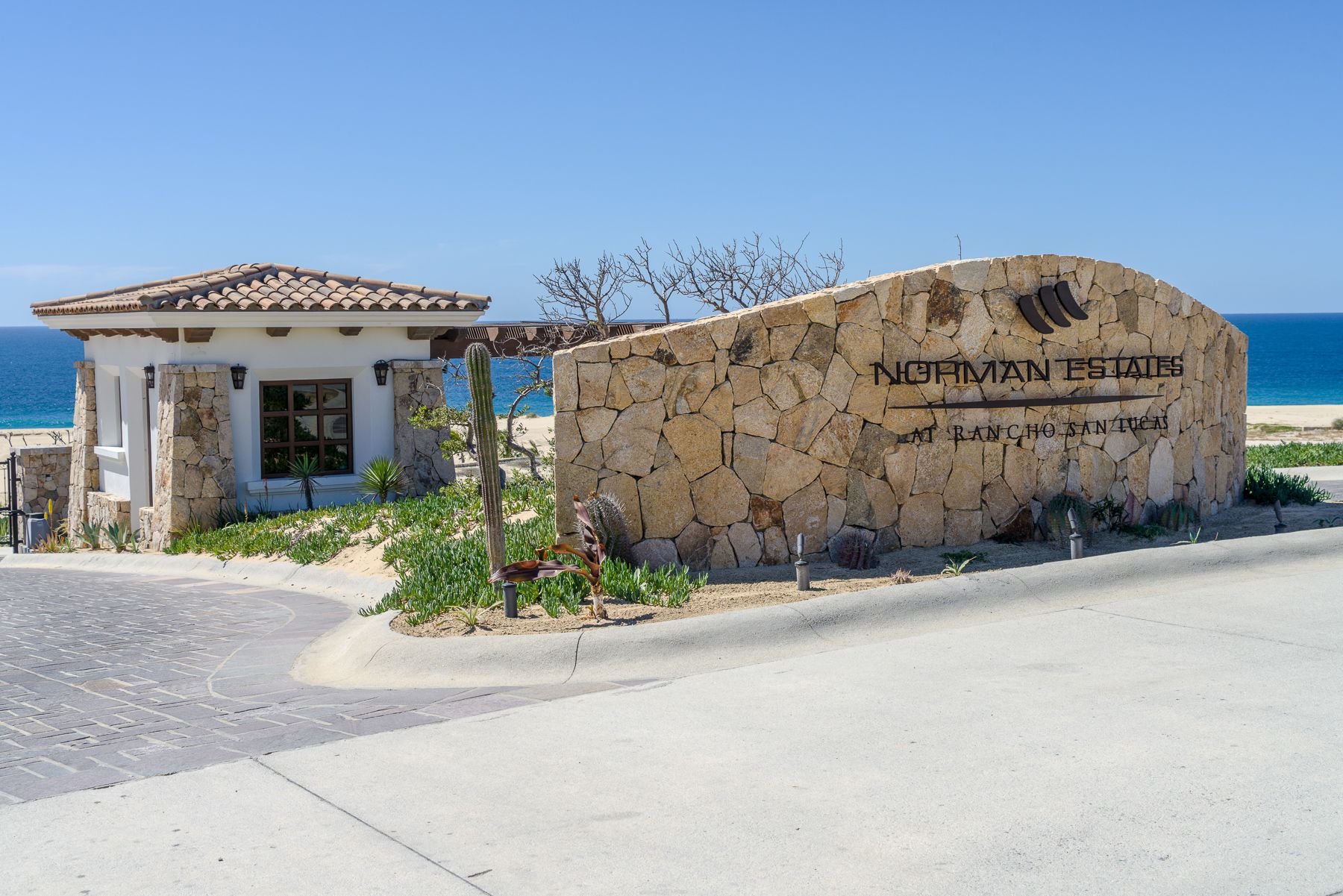 A scenic coastal view of a Mediterranean beach with stone buildings and turquoise waters stretching to the horizon.