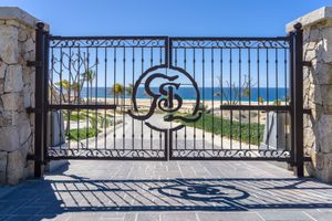 Wrought iron gate frames a scenic ocean view with white sand beach and blue waters beyond.