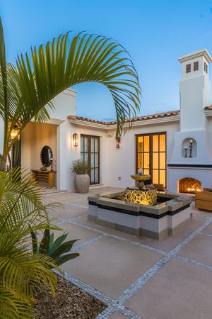 Mediterranean-style white villa exterior with palm trees, stone pathways, and warm evening lighting.