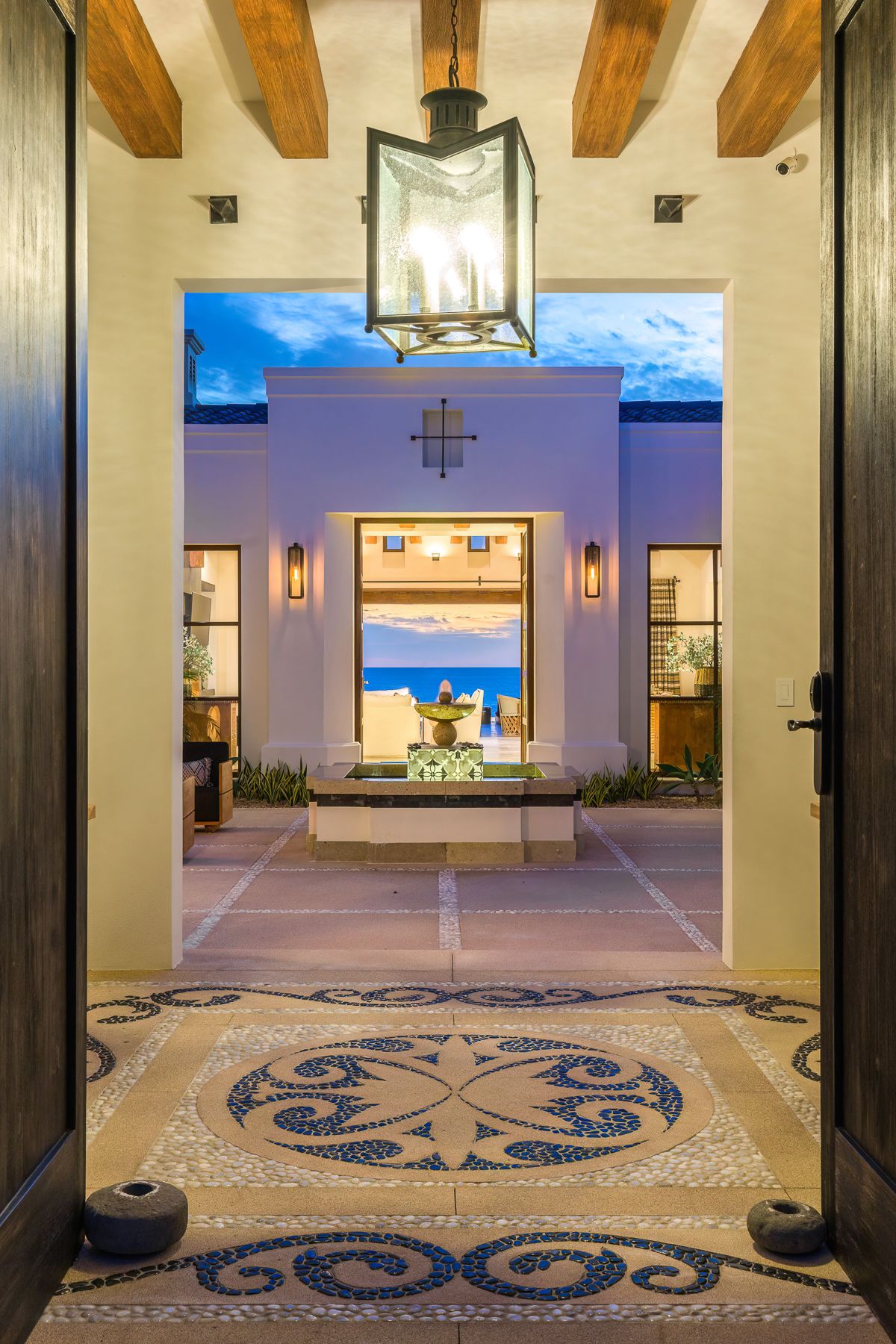 Elegant entryway with wooden beams and ornate octopus mosaic floor pattern leading to ocean views.