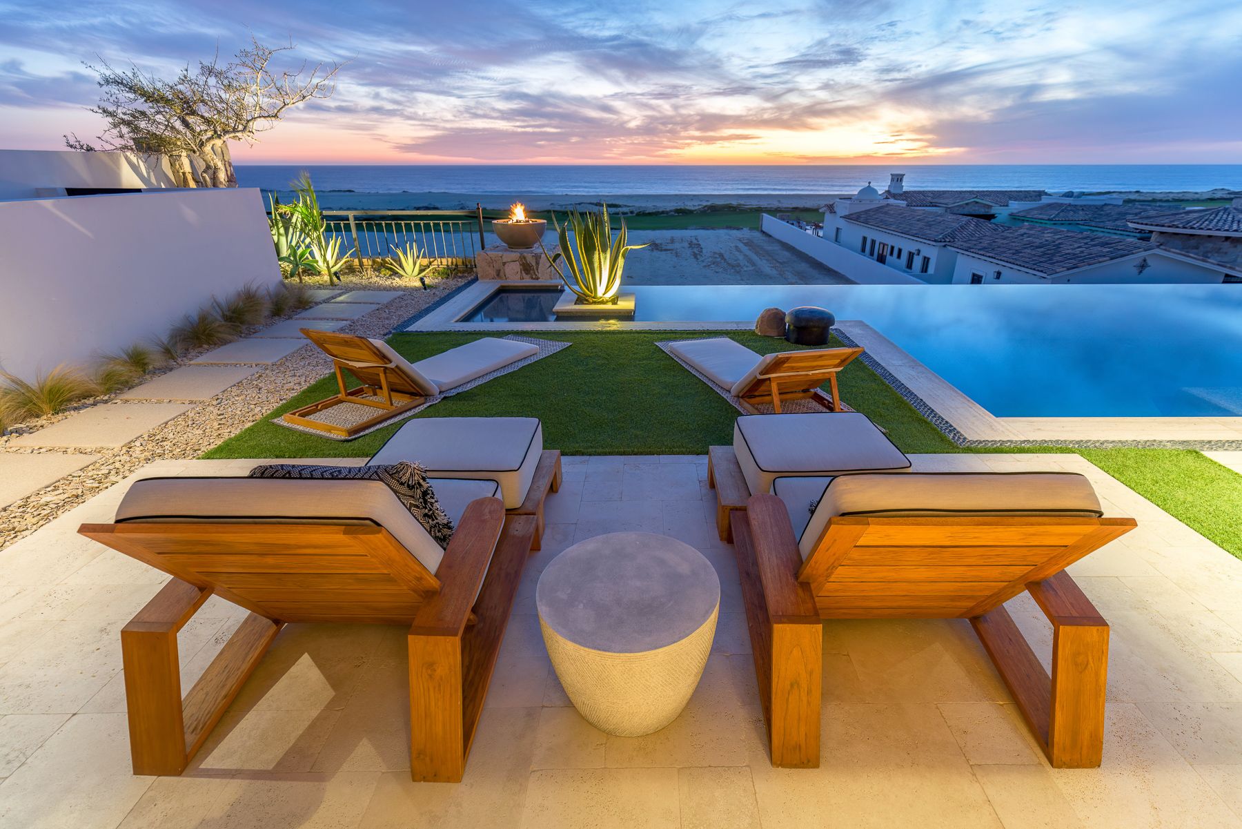 Wooden lounge chairs line up along an oceanfront infinity pool at sunset with panoramic coastal views.
