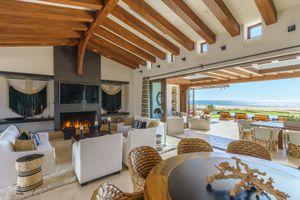 Modern coastal living room with exposed wooden beams and panoramic ocean views features contemporary white furnishings.