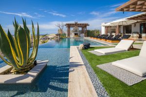 Luxury resort infinity pool with lounge chairs overlooking desert landscape and mountains under bright blue sky.