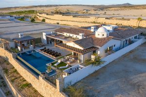 Aerial view of luxury desert villa with swimming pool and stone walls surrounded by arid landscape at sunset.