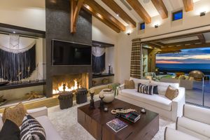 Luxurious modern mountain home interior features exposed wooden beams, stone fireplace, and panoramic windows with scenic views.