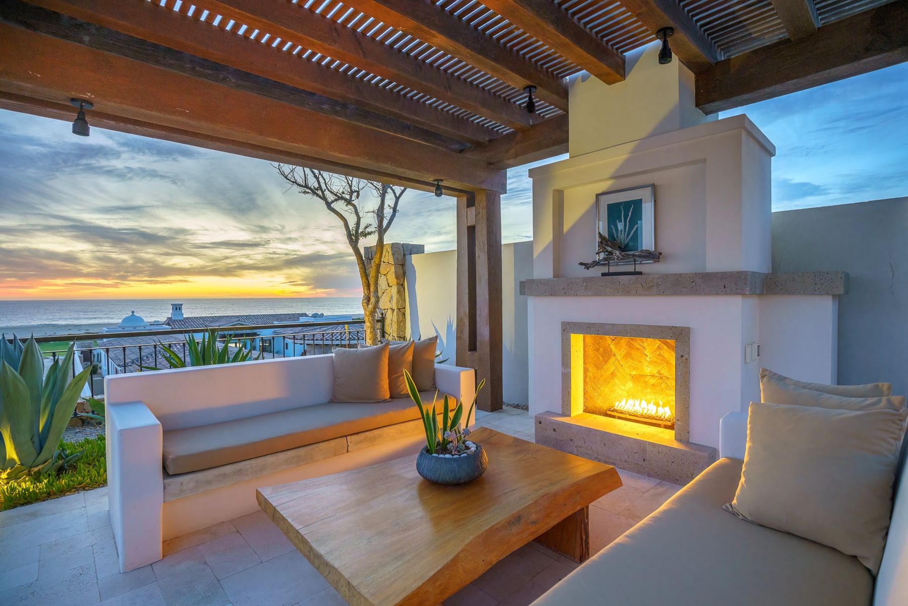 Modern covered patio with wooden pergola and built-in seating overlooking ocean views at sunset.