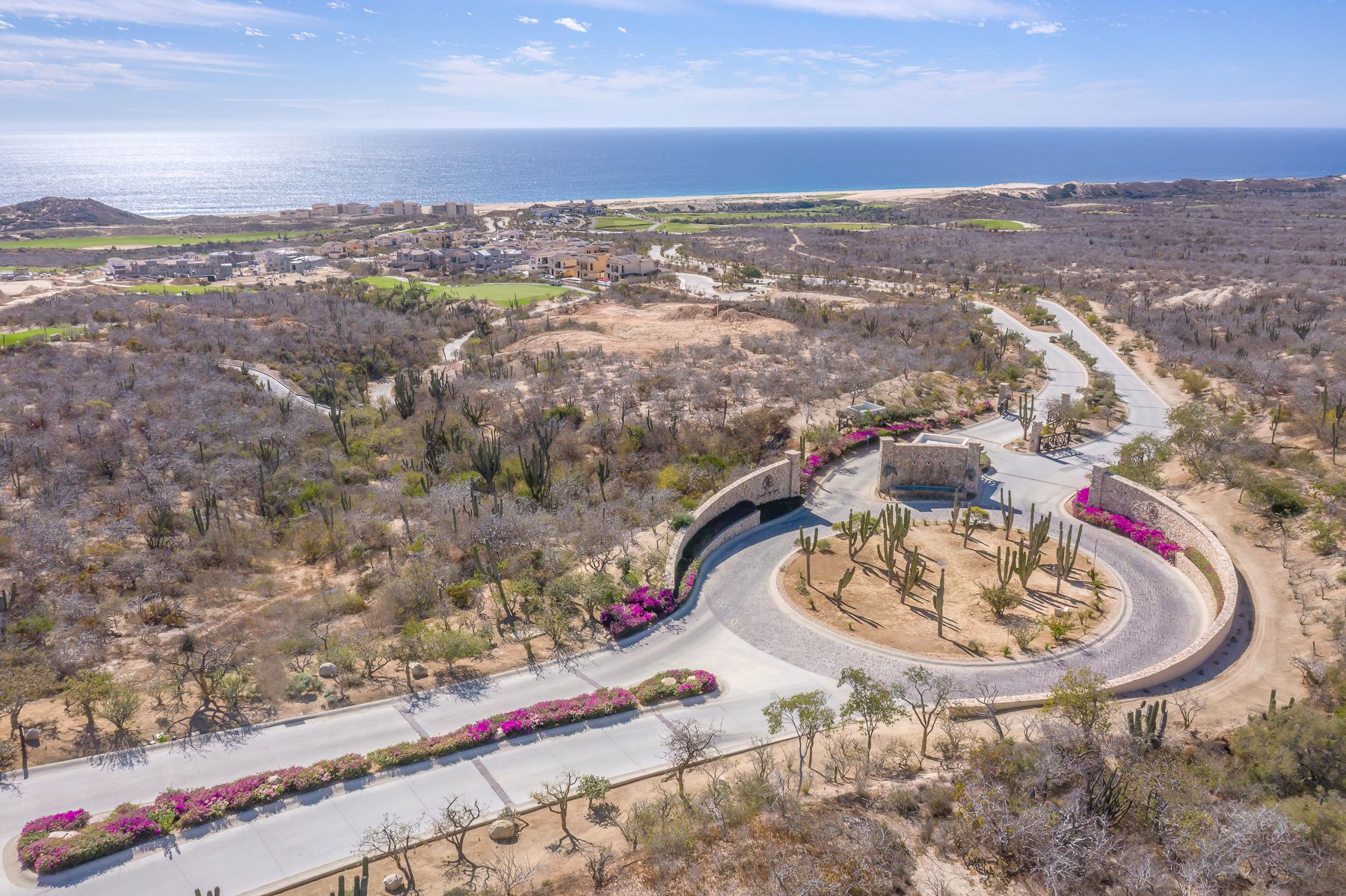 Aerial panoramic view of a winding mountain road with desert landscape and ocean in the distance.