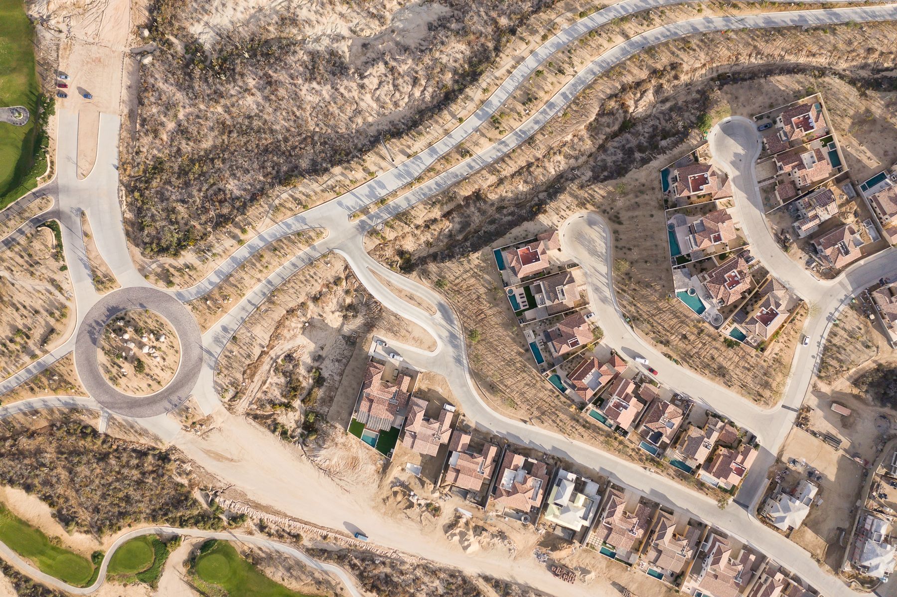 Aerial view of a curved residential street with houses and construction development in a hillside neighborhood.
