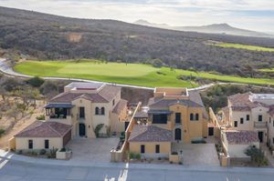 Aerial view of Mediterranean-style homes overlooking a lush green golf course against a rugged hillside landscape.