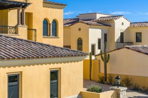 Mediterranean style homes with yellow stucco walls, terracotta tile roofs, and a tall cactus in the desert landscape.