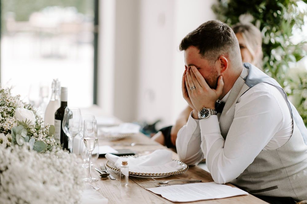 Someone appears emotional with hands covering their face at an elegant table setting decorated with white flowers.