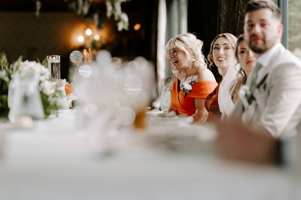 Wedding guests share a candid moment of laughter during a reception dinner at an elegant table setting.