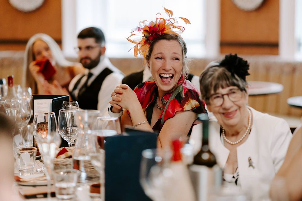 Wedding guests share joyful laughter and conversation while dining at elegant tables with wine glasses.