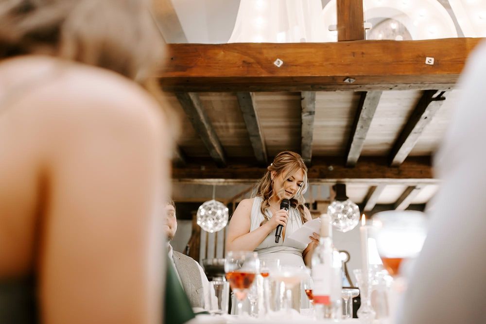 A rustic barn wedding reception venue with exposed wooden beams and elegant chandeliers hanging from the ceiling.