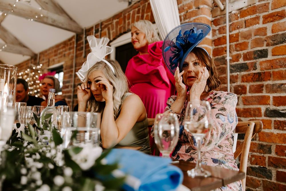 A group of people in formal attire raise wine glasses for a celebratory toast at a rustic brick-walled venue.