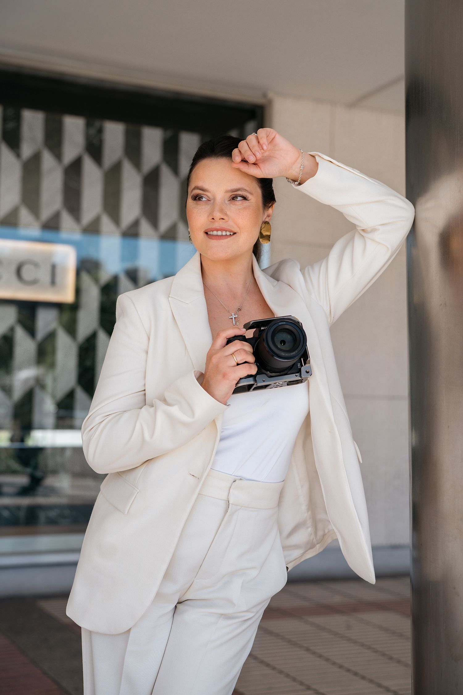 Professional wearing a crisp white blazer and shirt poses with a camera in an urban setting.