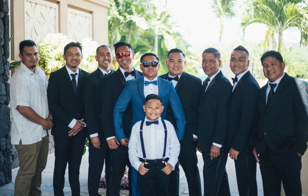 Wedding party in formal attire poses together outdoors with palm trees in the background.