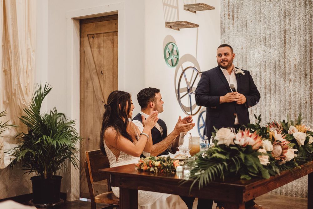 Wedding guests gathered around wooden tables during reception toasts and speeches.