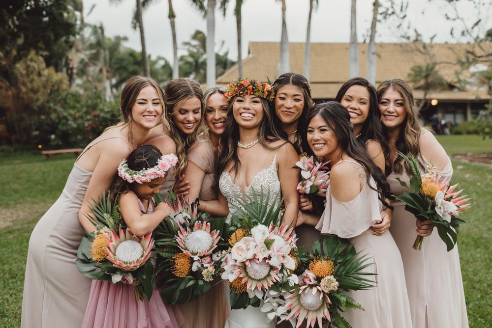 Bridal party in light pink dresses poses with tropical bouquets outdoors.