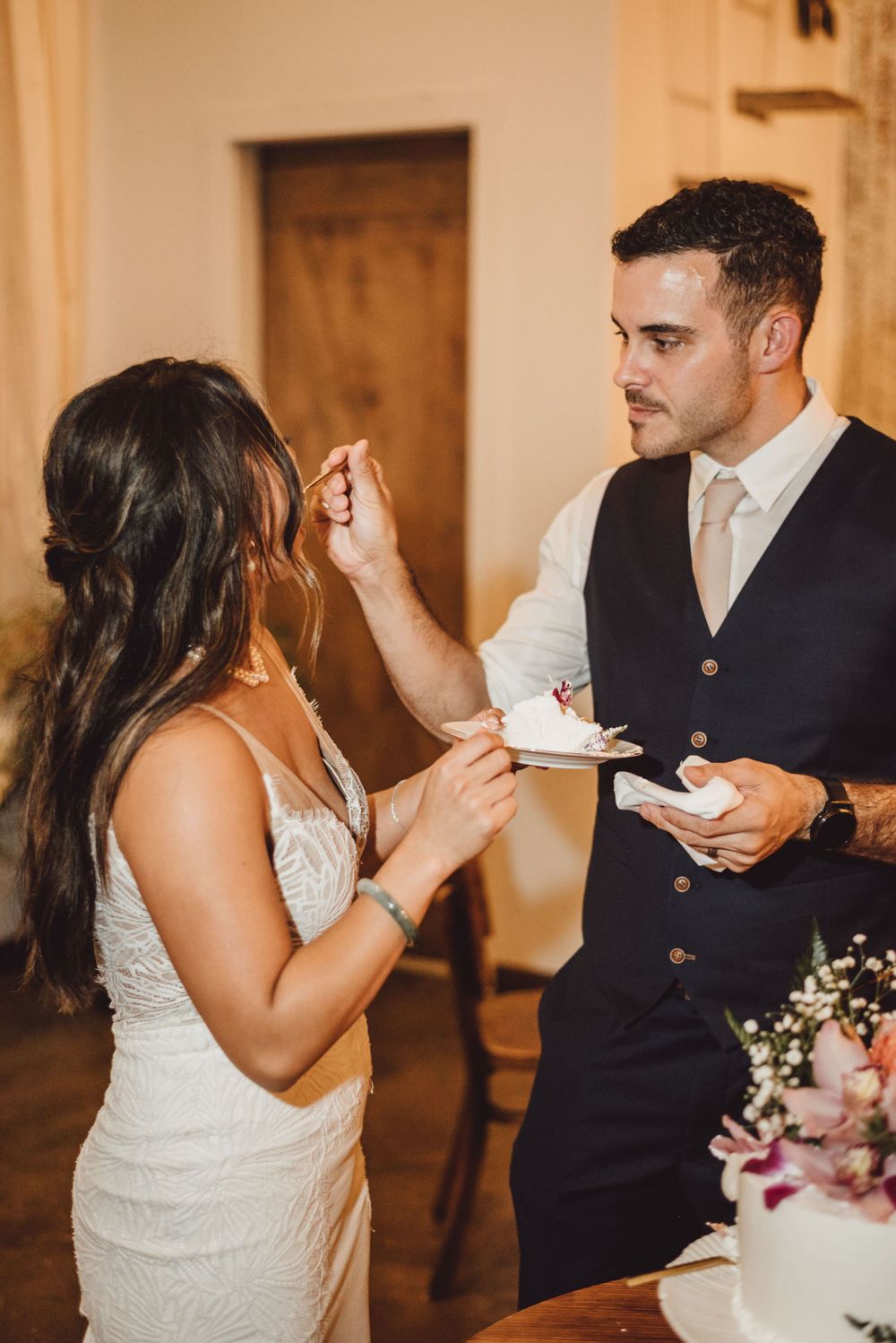 Newlyweds playfully feed each other cake during traditional wedding cake cutting ceremony.