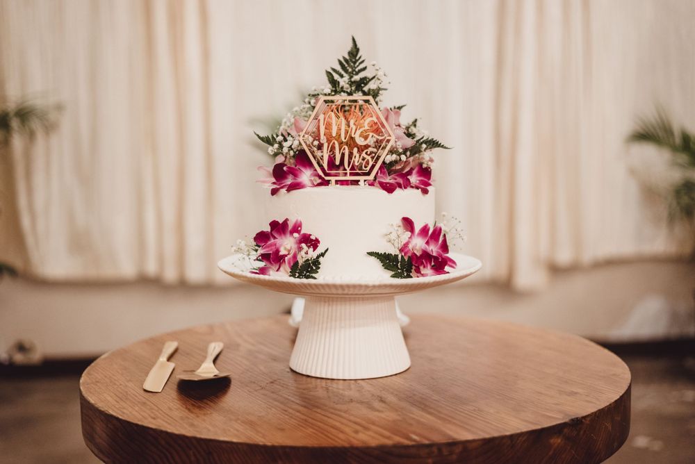 Elegant white wedding cake displayed on wooden table with pink floral decorations.
