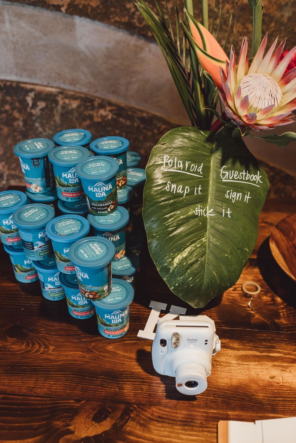 Wedding reception detail showing blue yogurt favors and tropical decor on wooden table.