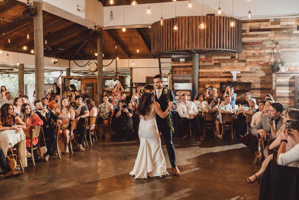 Wedding guests dance and celebrate together on a rustic wooden dance floor at an indoor reception venue.