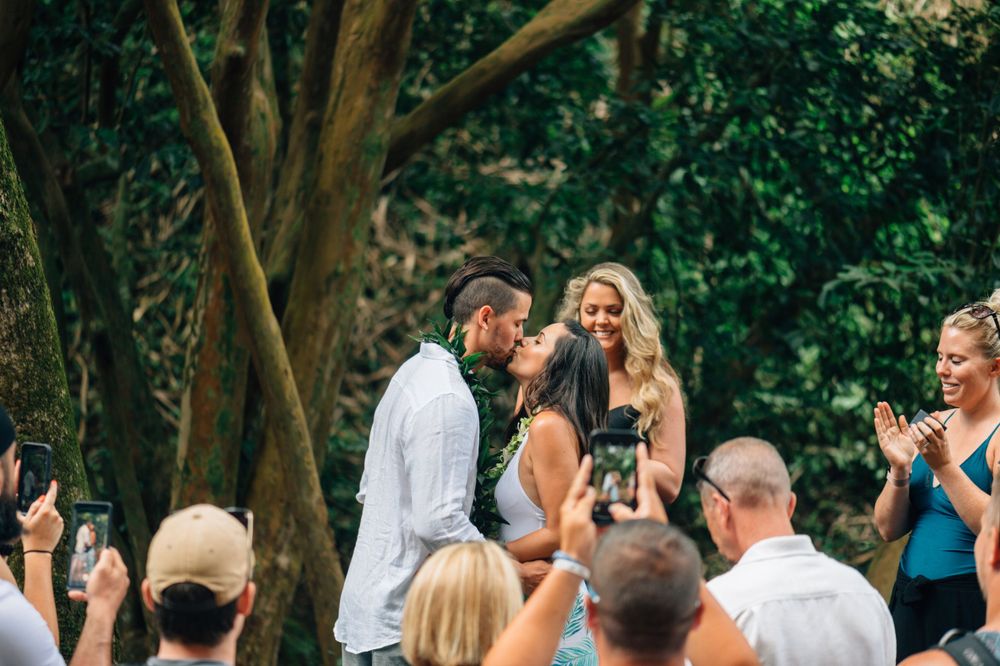 A joyful outdoor celebration with guests watching and taking photos in a wooded area.
