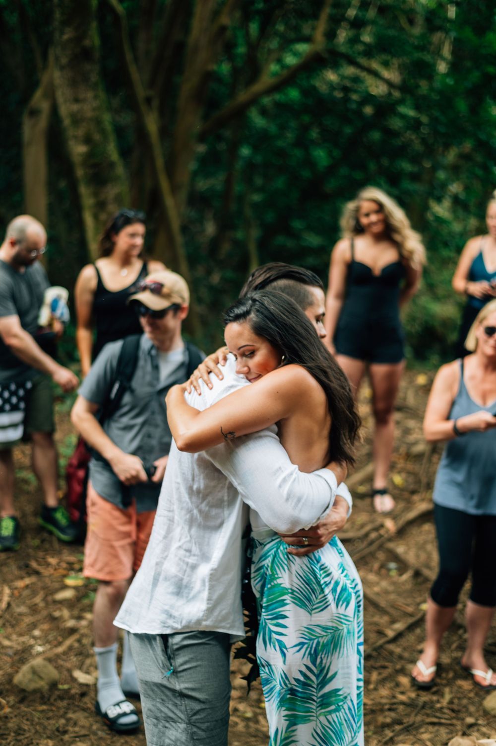 An emotional embrace during an outdoor ceremony while guests look on in a forest setting.