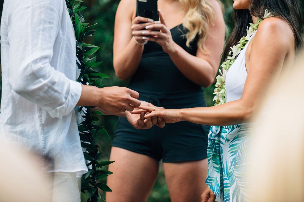 A close-up of hands exchanging rings during an outdoor ceremony in a forest.