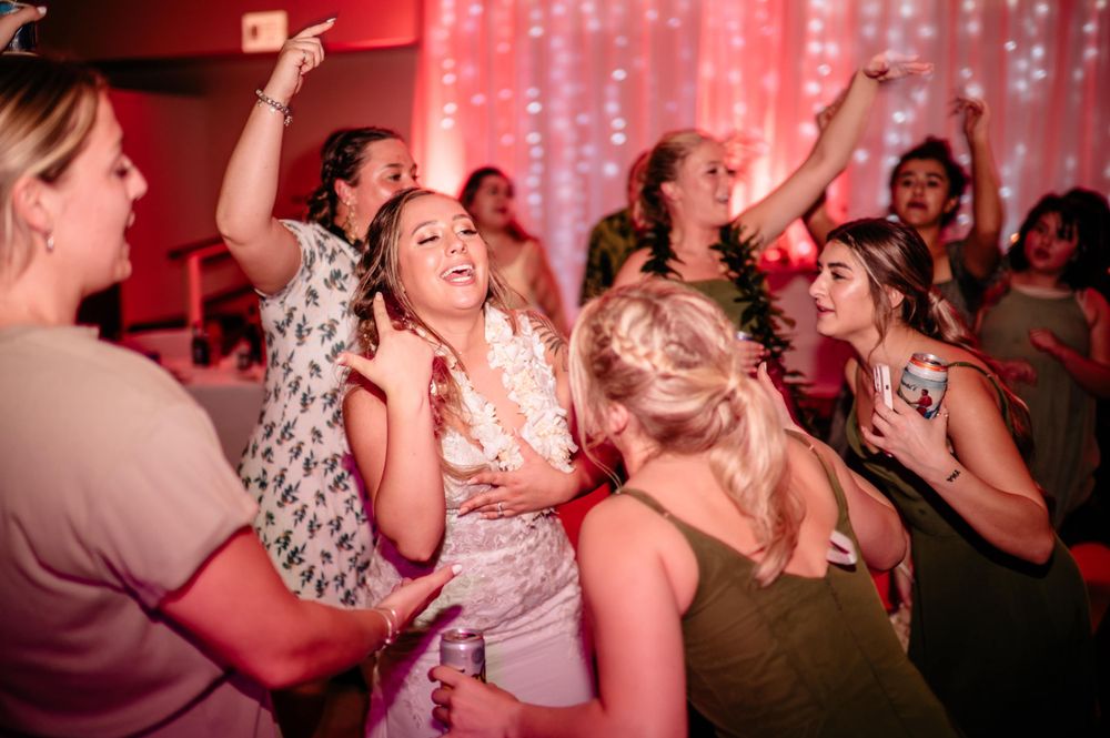 Wedding guests dancing and celebrating on the dance floor with pink lighting and decorative backdrop.