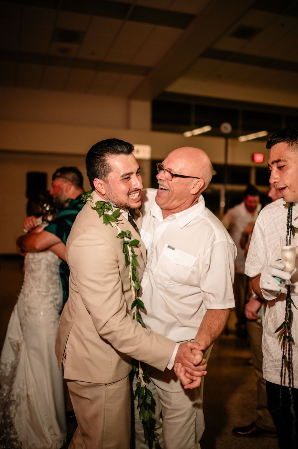 Heartwarming moment shared between wedding guests wearing traditional Hawaiian leis at reception.