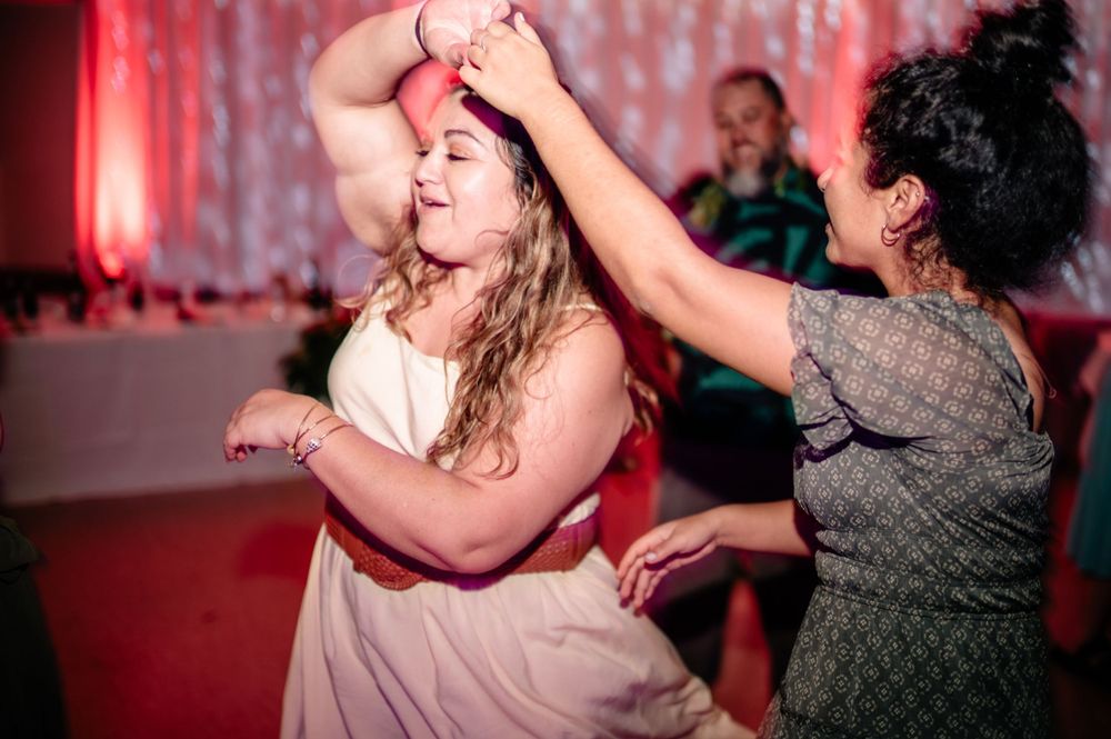 Wedding guests dance energetically under pink lighting at reception celebration.