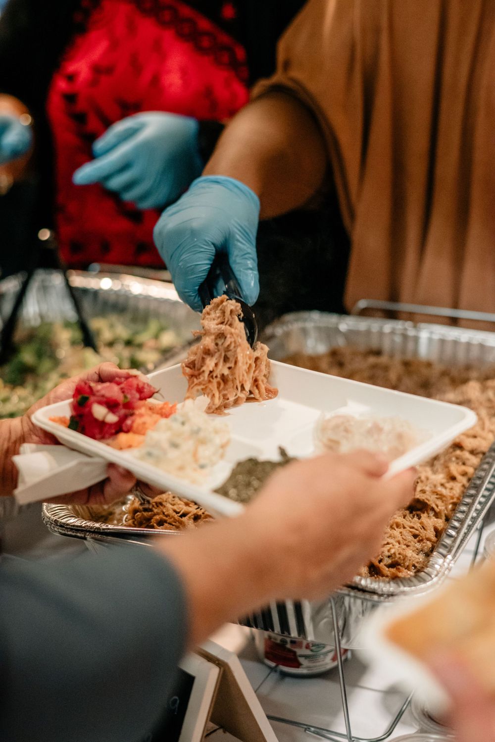 Catering staff serving food at a buffet line wearing protective gloves.