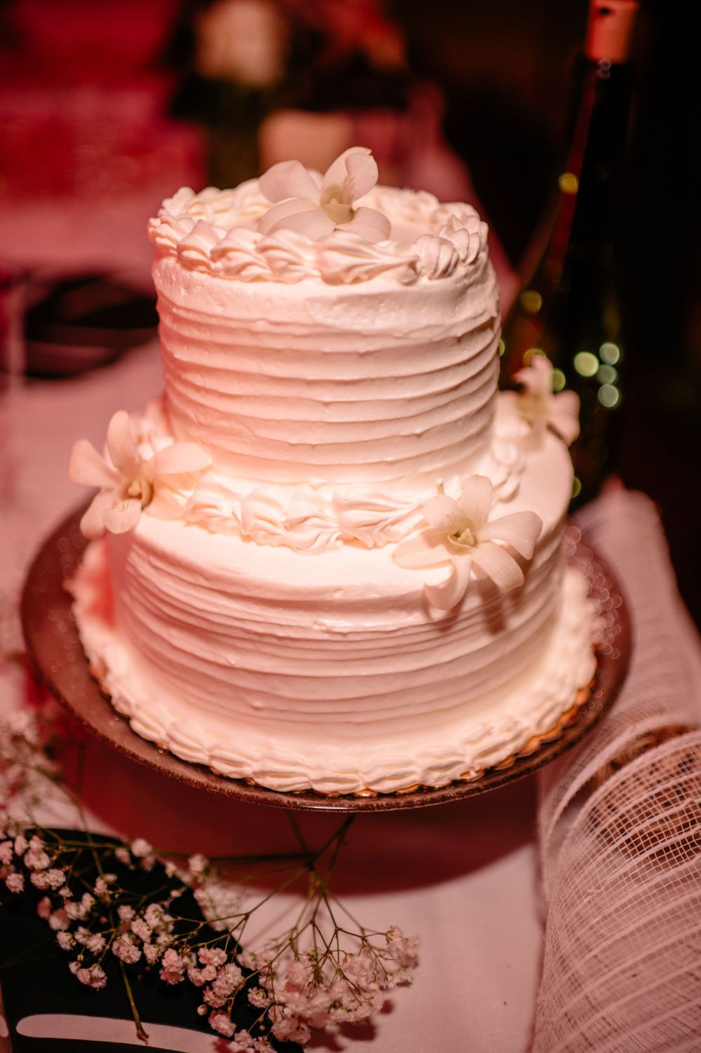 Two-tiered white wedding cake with delicate floral decorations and textured frosting.