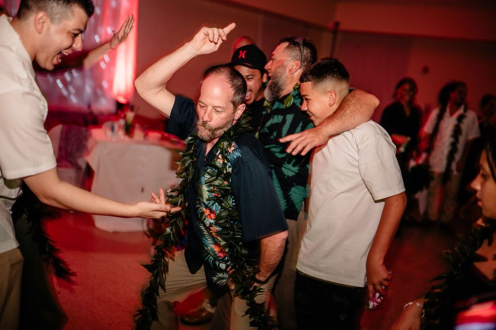 Wedding guests dance and celebrate with traditional Hawaiian leis at reception party.