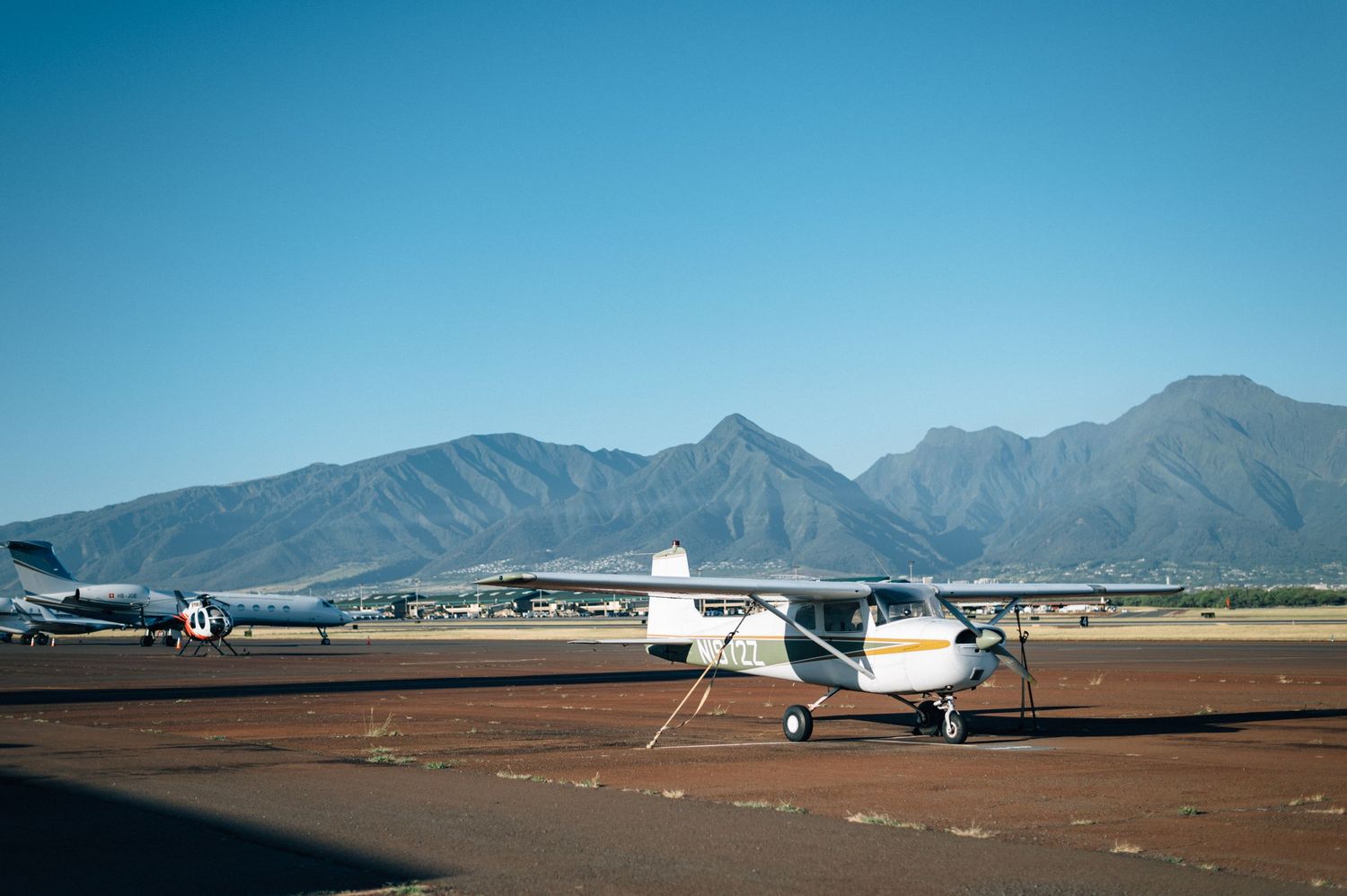 Small aircraft and hangars lined up at an airport with mountain ranges visible in the distance.