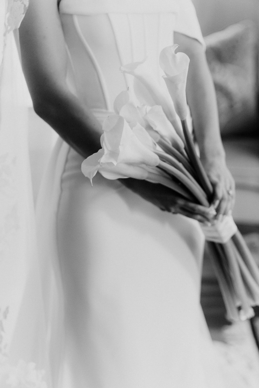 Black and white close-up of bride in white dress holding elegant calla lily bouquet.