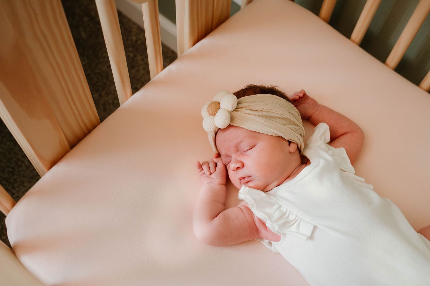 Sleeping newborn wrapped in white blanket on pink bedding.