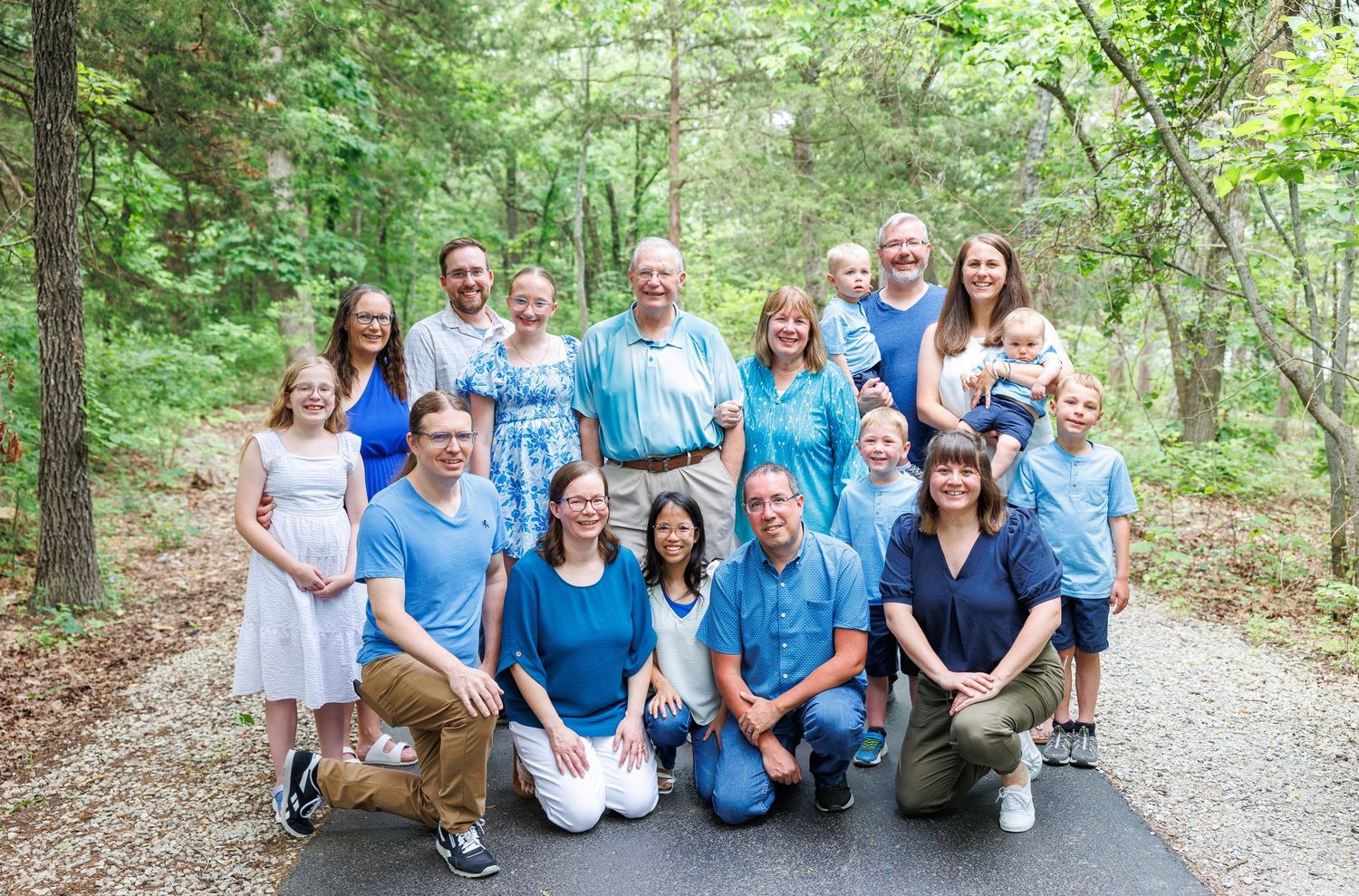 Large family group wearing coordinated blue outfits poses together on a wooded path in Branson, Missouri taking family photos.
