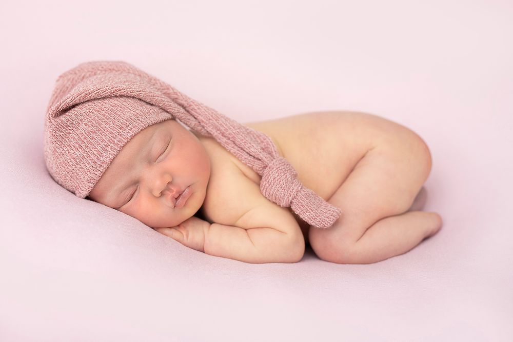 Newborn baby girl poses with just sleepy had in pink