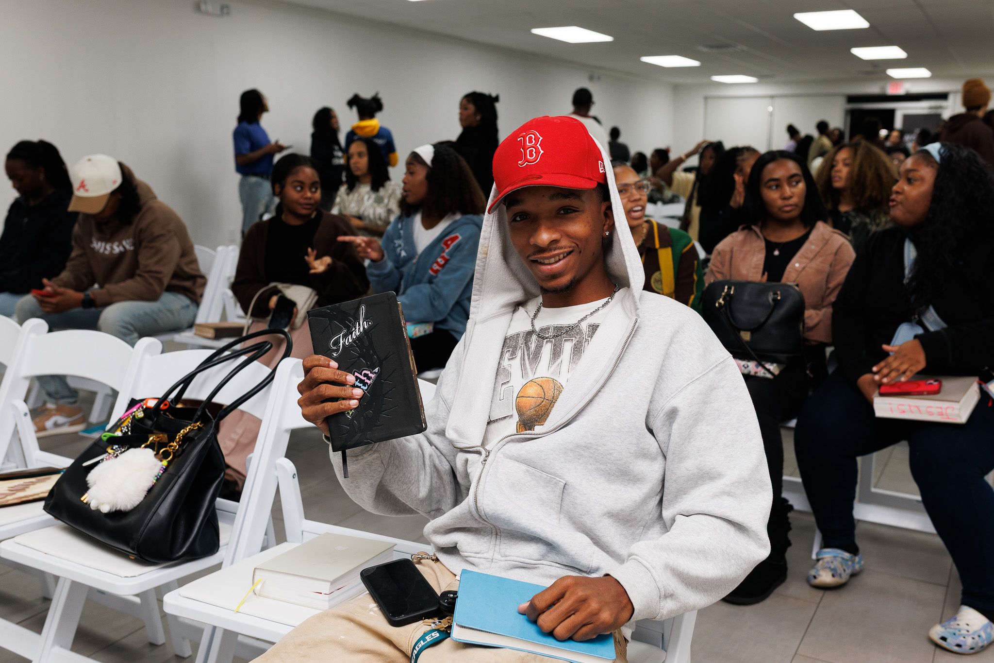 Students sit in a classroom with phones and study materials while wearing casual attire and baseball caps.
