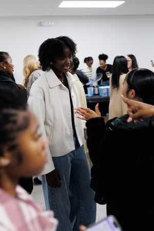 People standing in line at an indoor event wearing business casual attire in a brightly lit room.