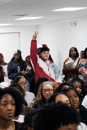 A crowded room filled with attendees standing against a white wall at an indoor gathering.