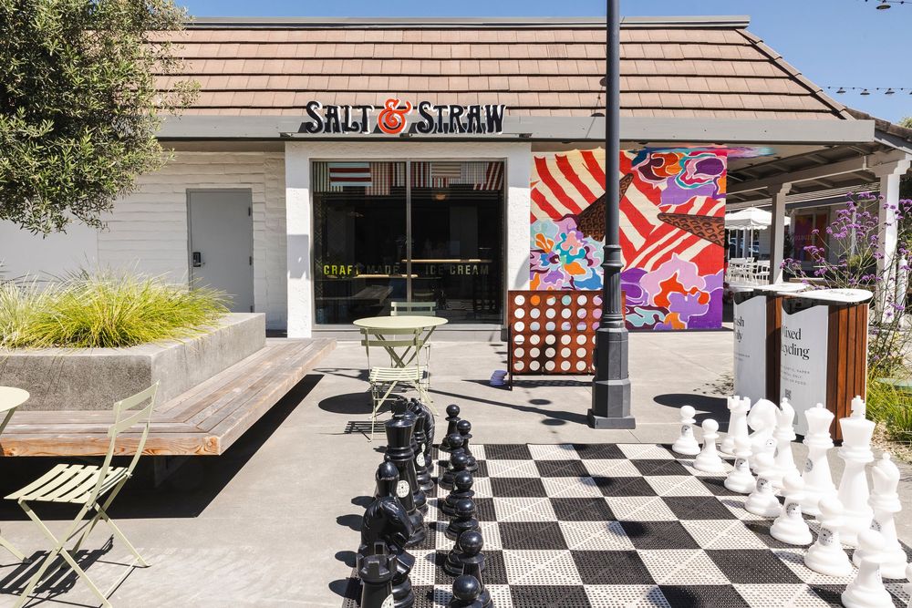 A large outdoor chess set with black and white pieces on a patio near a storefront.