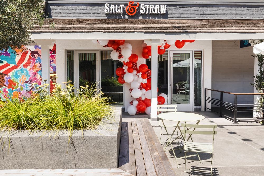 A storefront decorated with red and white balloons features a Salt & Straw ice cream shop entrance with outdoor seating.
