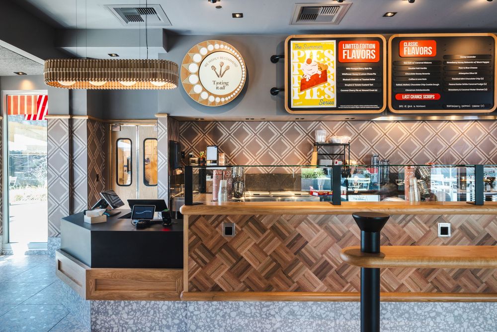 Modern fast food restaurant interior with wooden herringbone wall panels and digital menu boards above the counter.